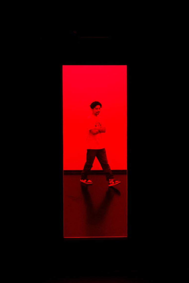 A guest stands with arms crossed in a red-lit doorway in Chromesthesia.