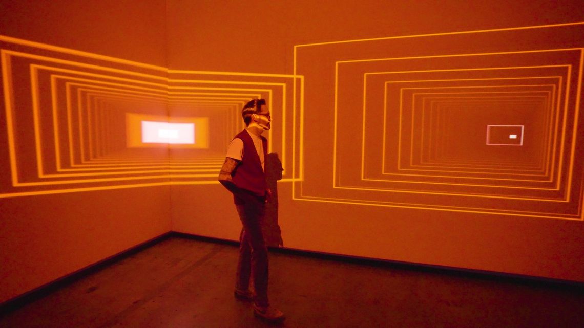 A guest standing in Onion Skin in orange, nested rectangles of light opening on either side of him.