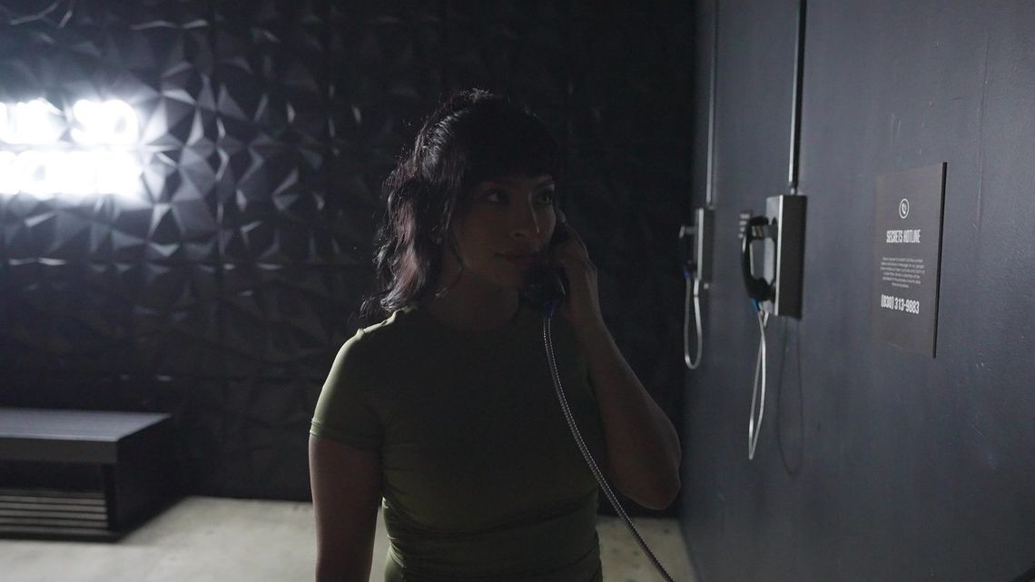 A guest listens on one of the Secrets phones, the neon glowing on the textured surface behind her.