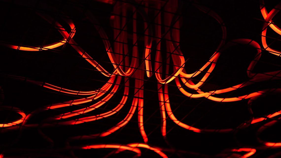 Directly under Medusa, glowing red tubes curving down from the chandelier toward the lens.