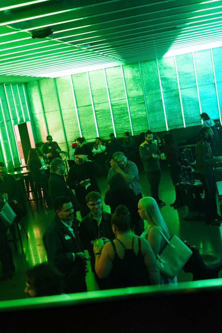 The Portland Lounge lit green from above, a crowd of guests on the floor beneath the tubes.