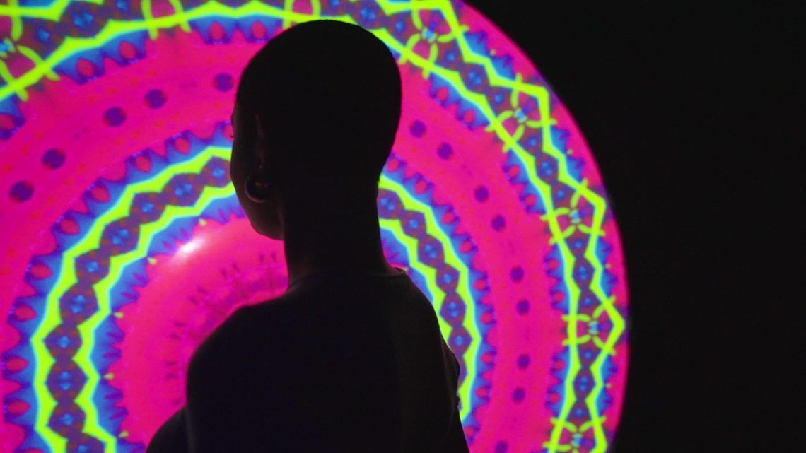 A guest in silhouette against the giant Light Portal disc, its kaleidoscope pattern blazing pink, lime and violet.