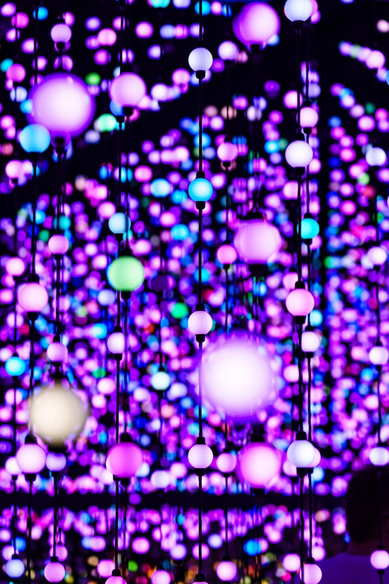 Close up of hanging bulbs in Unknown Atmospheres, glowing violet, pink, white and teal.