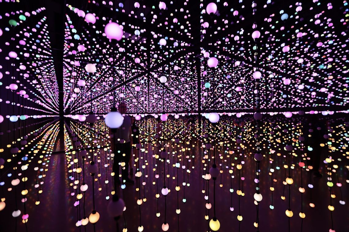 A guest walks through Unknown Atmospheres as rows of pink and gold bulbs hang all around.