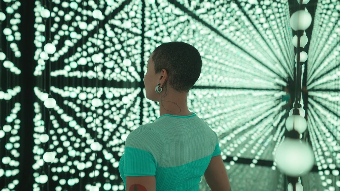 A guest in profile inside Unknown Atmospheres, San Antonio, surrounded by thousands of bulbs glowing white and teal.