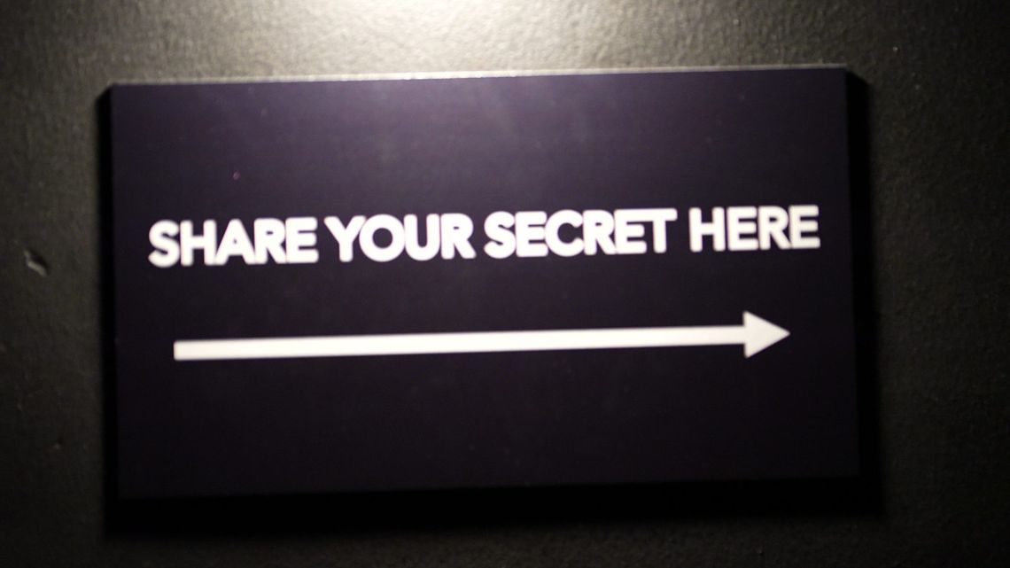A sign in the dark reading SHARE YOUR SECRET HERE, an arrow pointing the way.