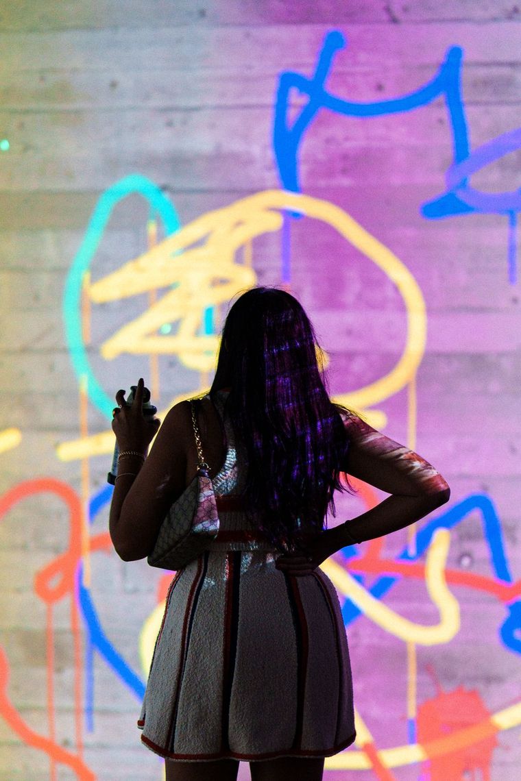 A guest holds a laser spray can before a wall of looping yellow, blue and orange lines in Laser Graffiti.