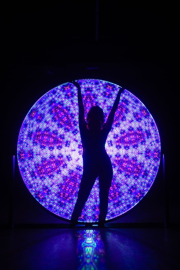 A guest in silhouette, arms raised, against a Light Portal disc patterned in violet and magenta.