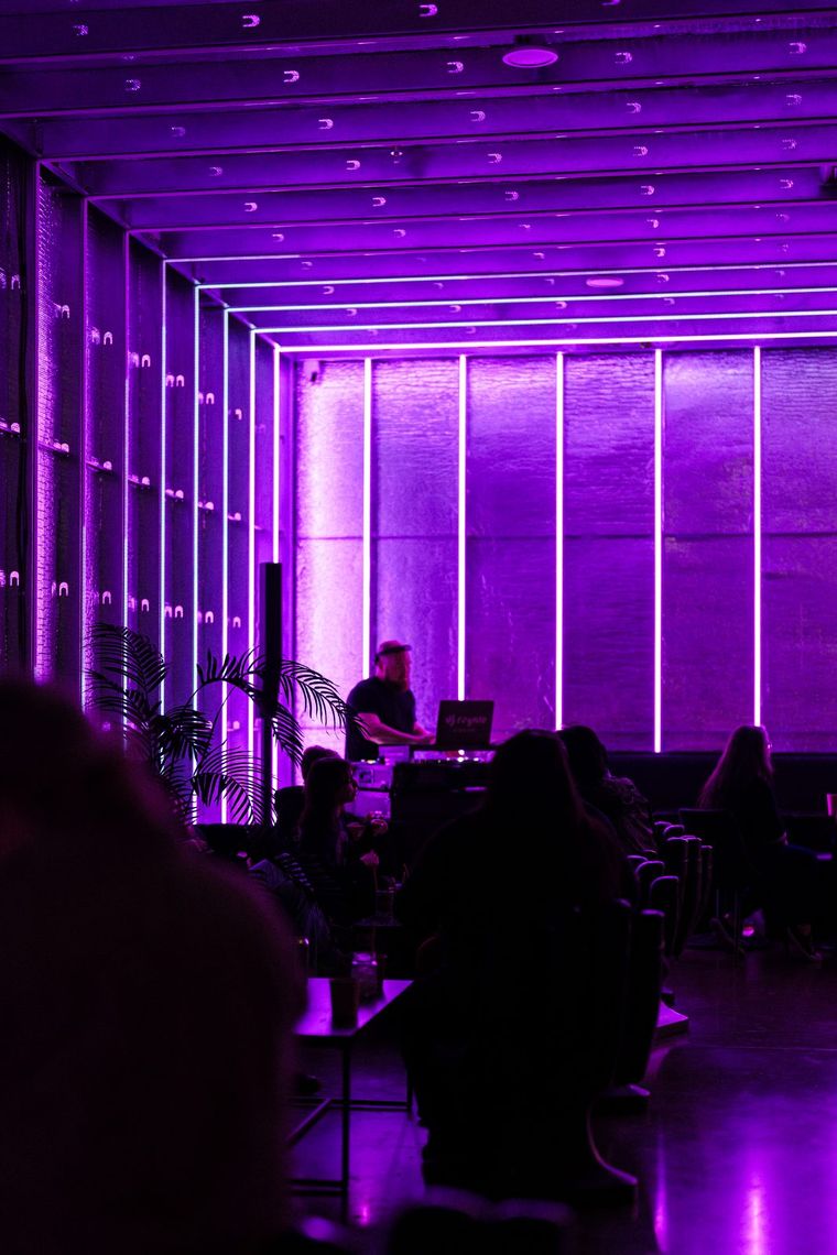 The Portland Lounge washed in violet, guests and a DJ at the far end under rows of tubes.