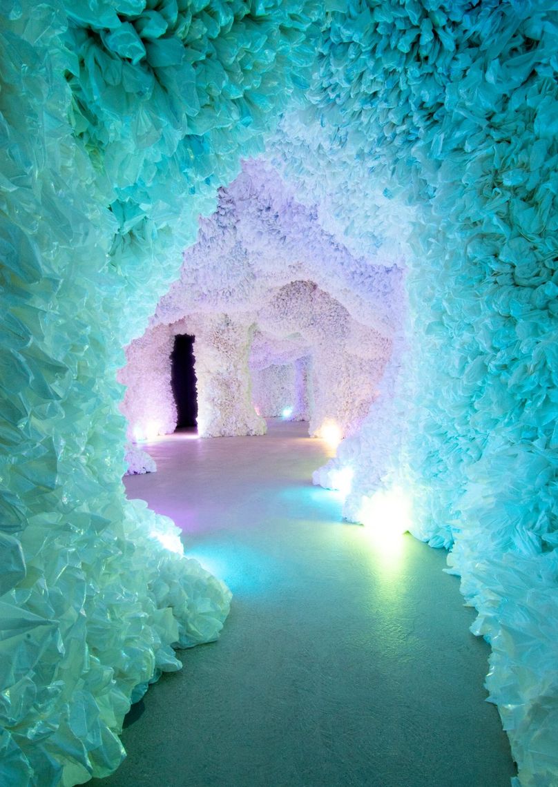A winding tunnel of the cave lit teal, the path traced by coloured lights.
