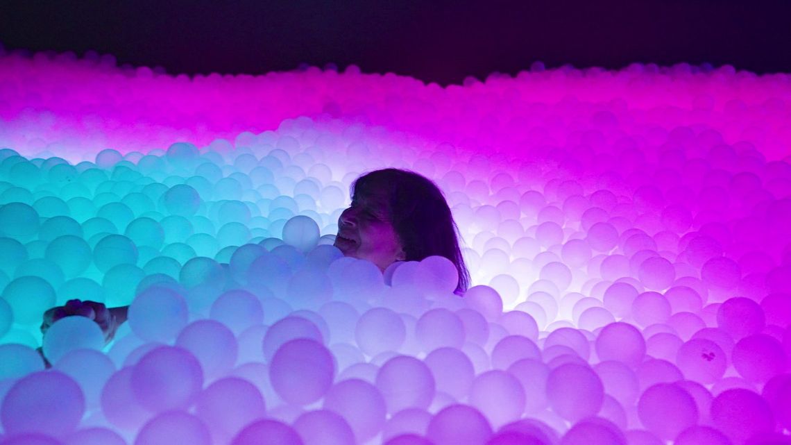 A guest smiles up from the pit, the balls around her glowing cyan, white and pink.