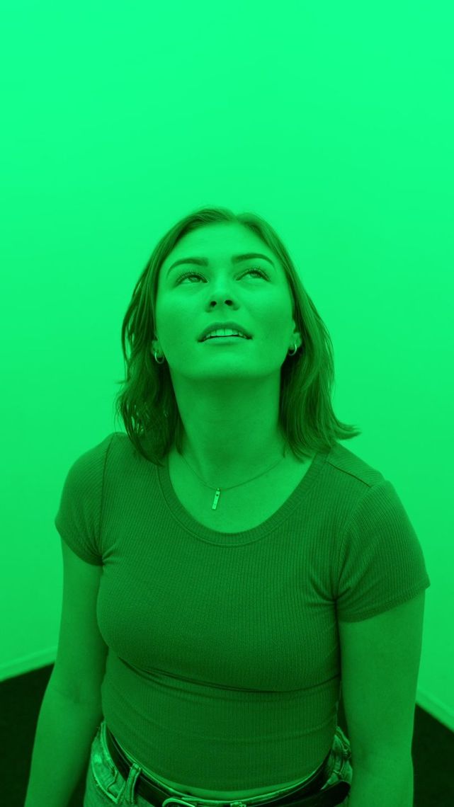 A guest inside the green chamber of Chromesthesia, face tipped up into the light, everything around her saturated green.