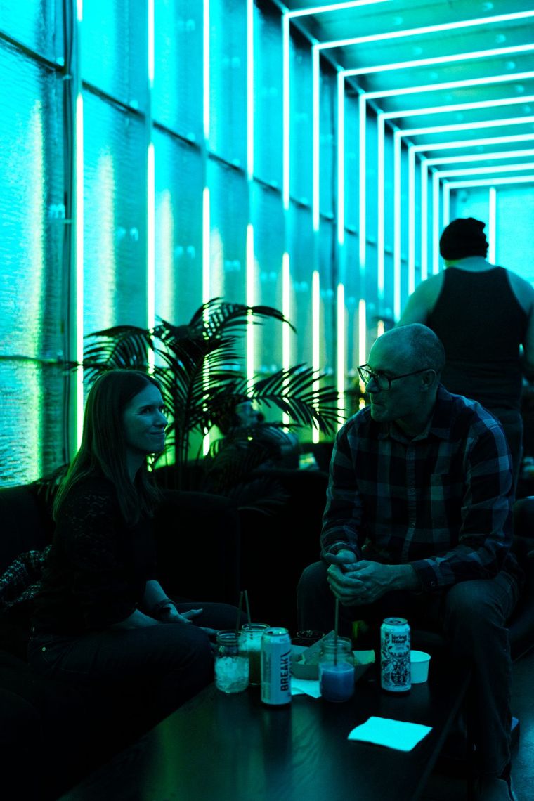 Guests on a sofa in the Portland Lounge, the tubes behind them glowing teal and cyan.