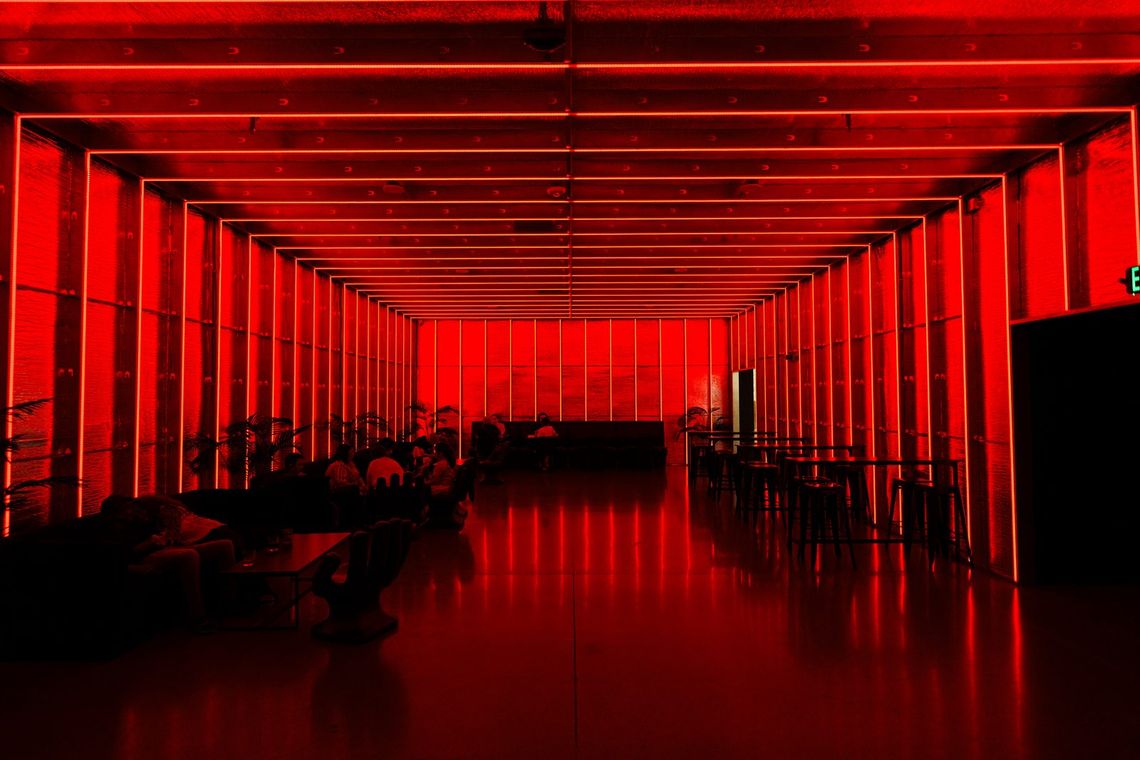 The Portland Lounge washed in red, frames of light lining the walls and ceiling, guests seated along the left.