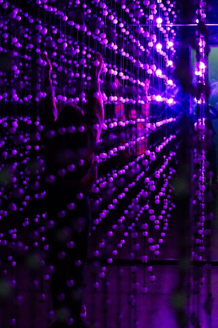 A guest reaches up between strands of glowing violet bulbs in Unknown Atmospheres.