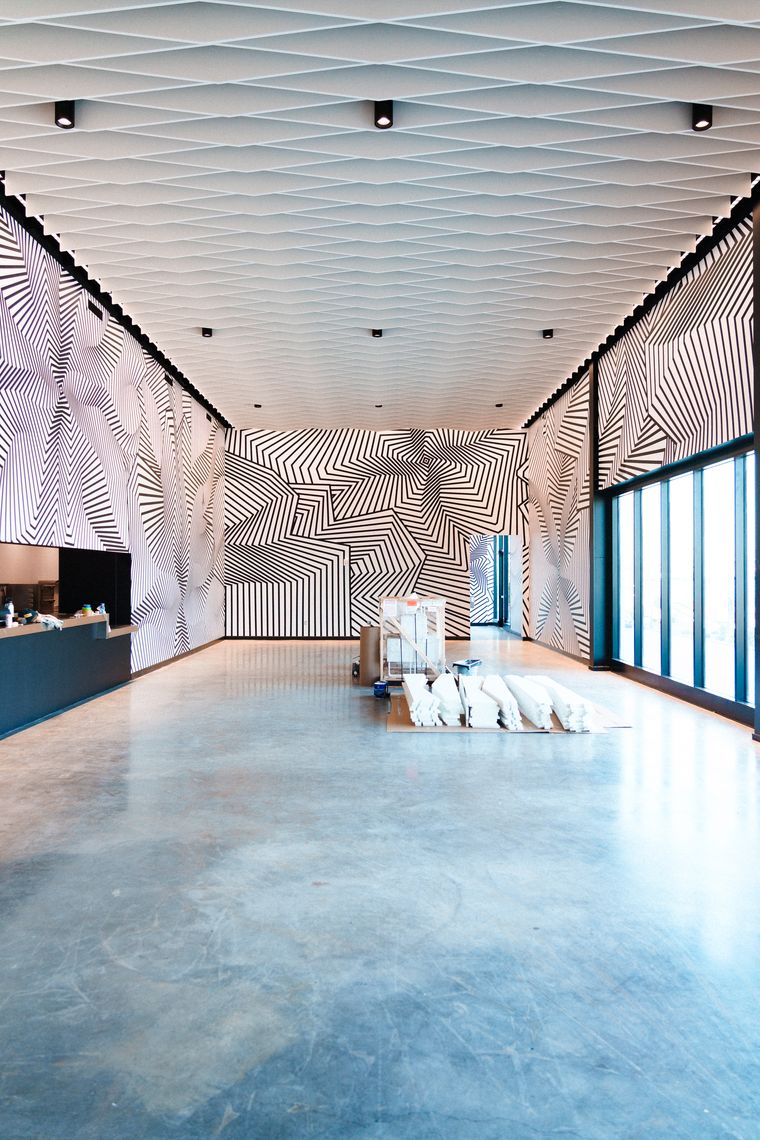 Black-and-white striped op art murals wrap the Los Angeles lounge walls beneath white ceiling panels, photographed during buildout.