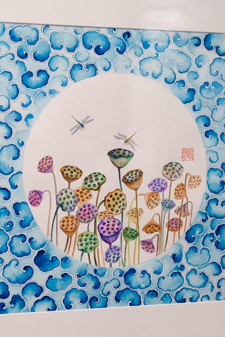 A watercolor by Ningshu Fang: lotus seed pods and two dragonflies in a white circle framed by blue clouds.