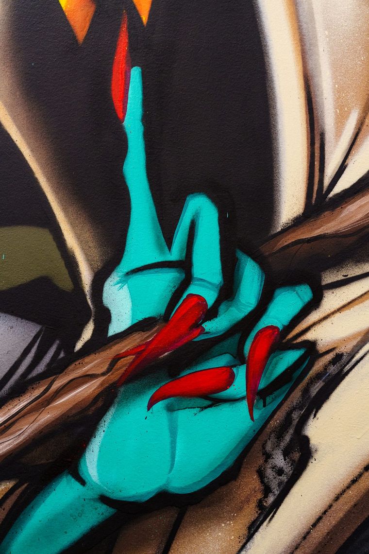 Close on a graffiti mural in Walls Within: a teal hand with red claws in spray paint.