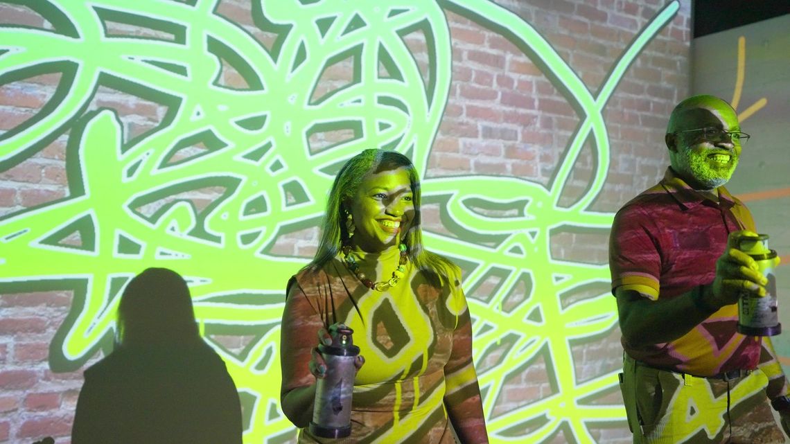 Two guests paint with light, lime green loops covering the projected brick.