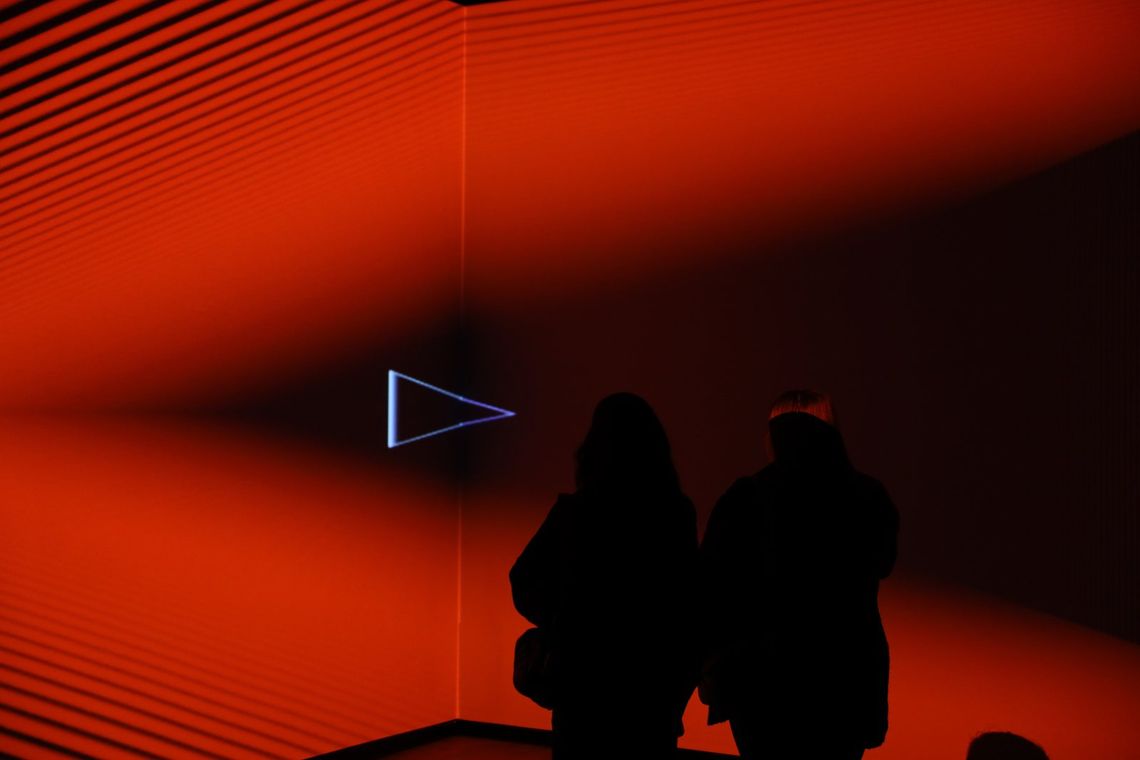 Two guests in silhouette against walls washed red and orange in Onion Skin, a small outlined triangle beside them.