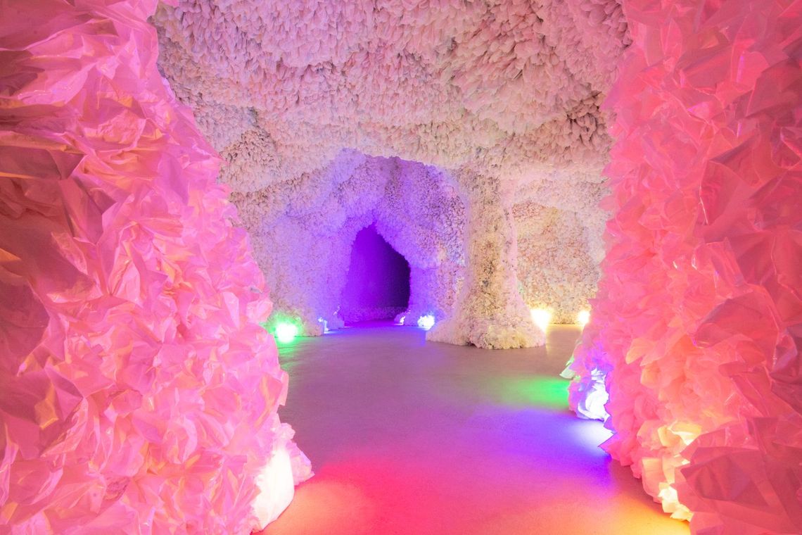 A Rainbow Cave passage glowing hot pink and violet, crinkled plastic walls framing a purple doorway ahead.