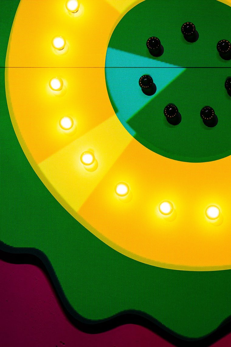 Close up of a yellow flower ringed with glowing bulbs, its green center studded with black knobs, in Are You There?