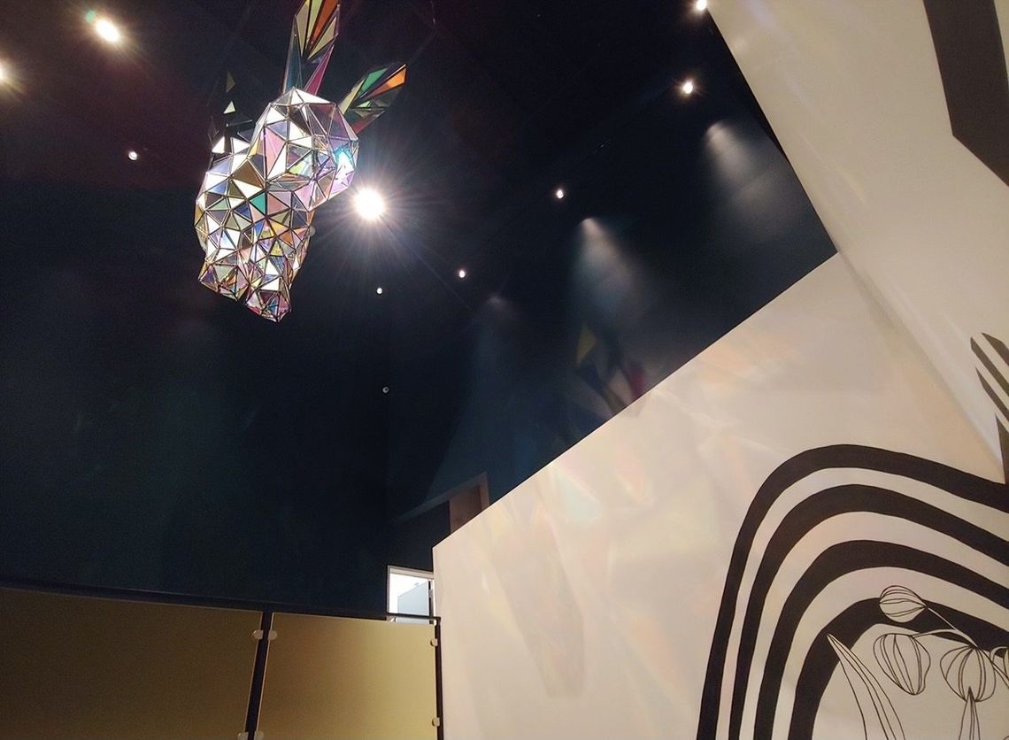 Looking up at Down the Rabbit Hole: the faceted rabbit hangs from the dark ceiling above the black and white mural.