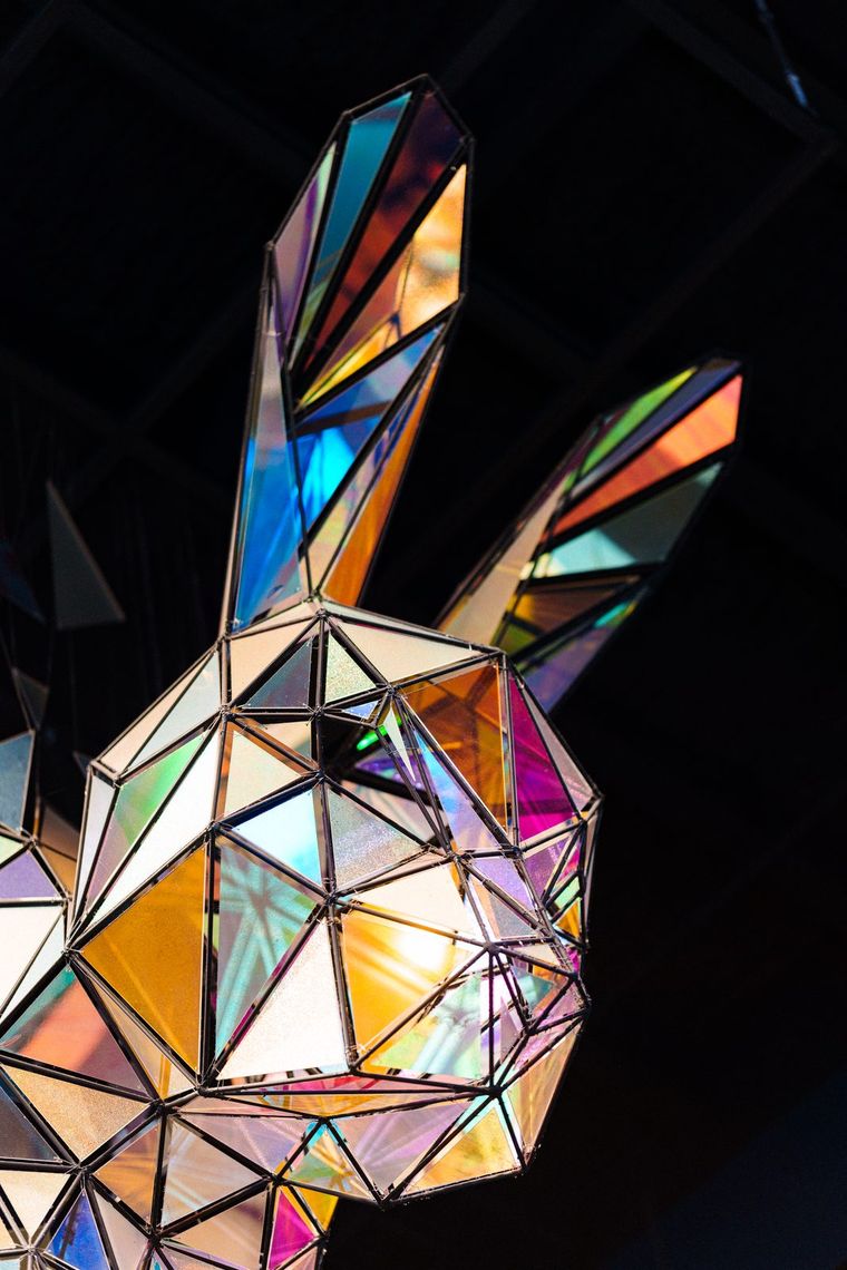 The iridescent sculpture seen from below, both faceted ears rising into the dark.