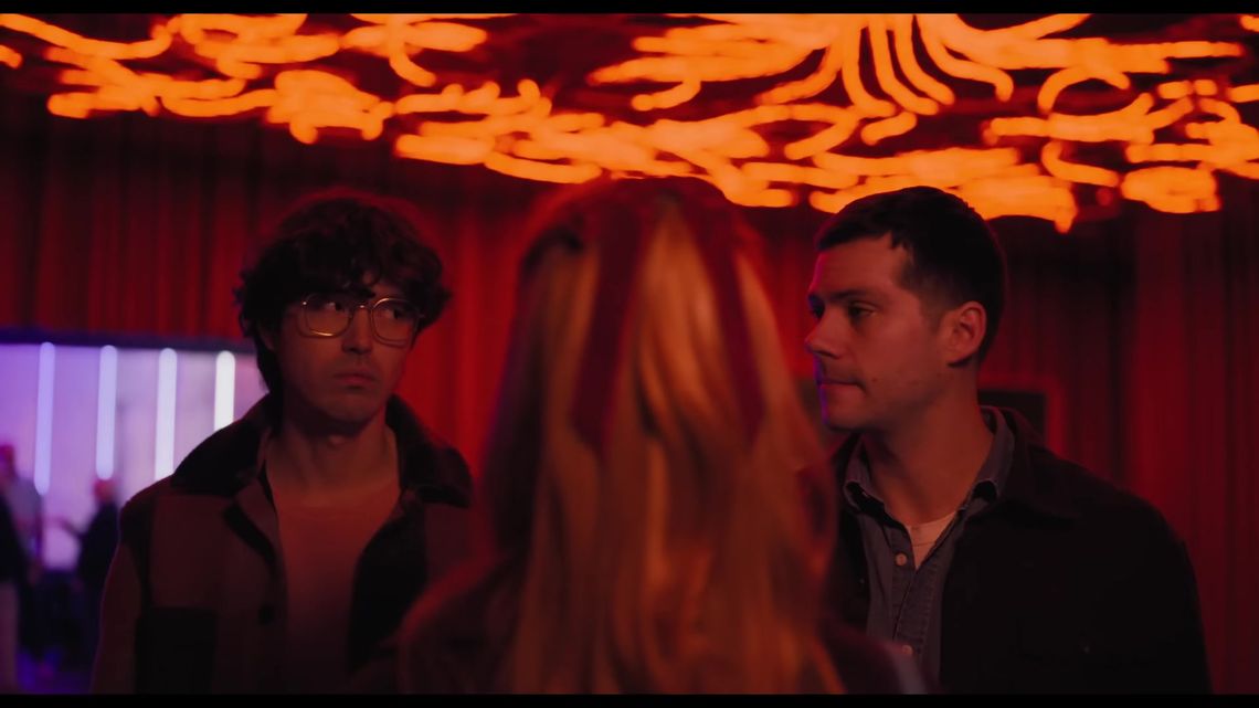 James Sweeney and Dylan O’Brien beneath the orange illuminated Medusa installation.