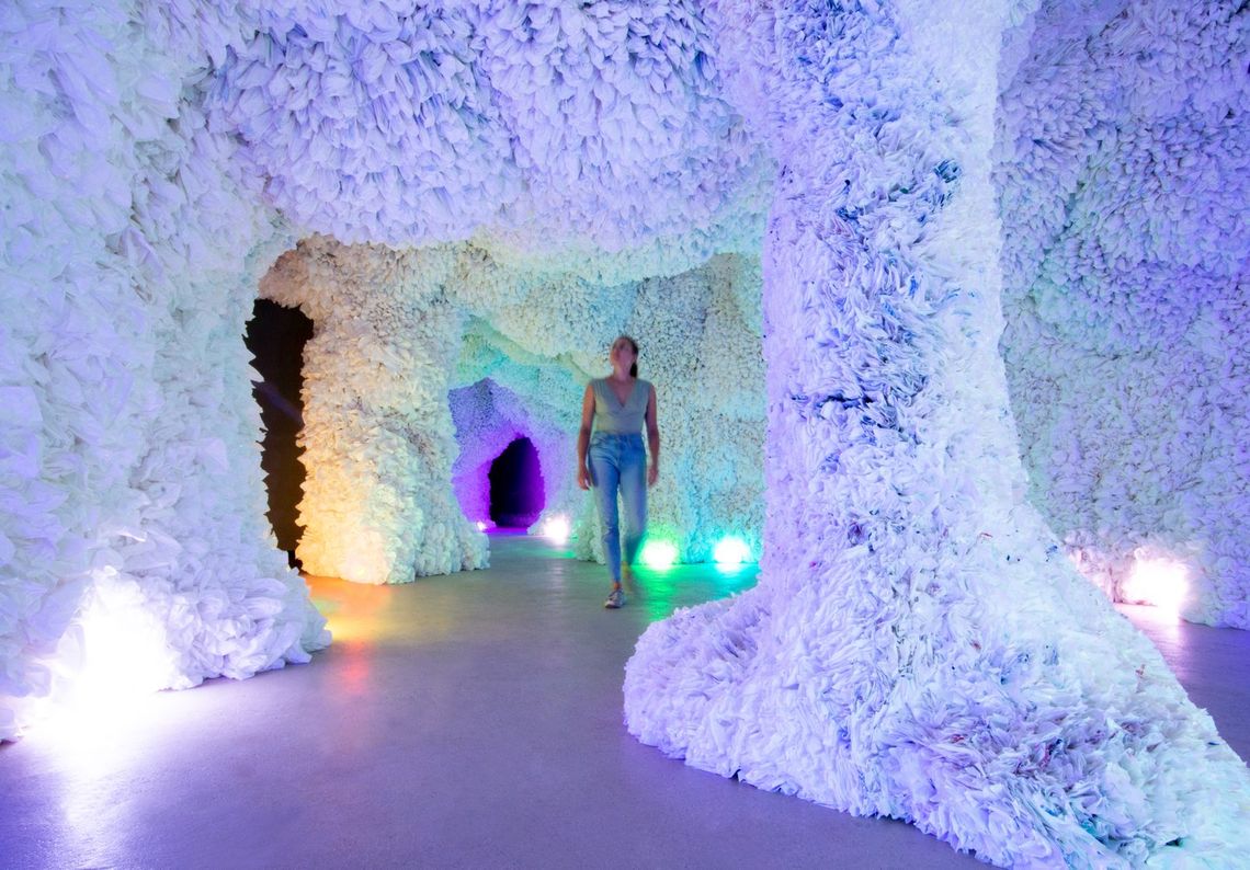 A guest walks between the white columns of the cave, coloured lights glowing along the floor.