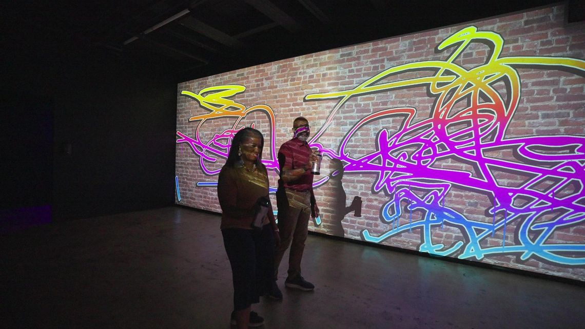 The whole projection scribbled in colour, two guests small in front of it.