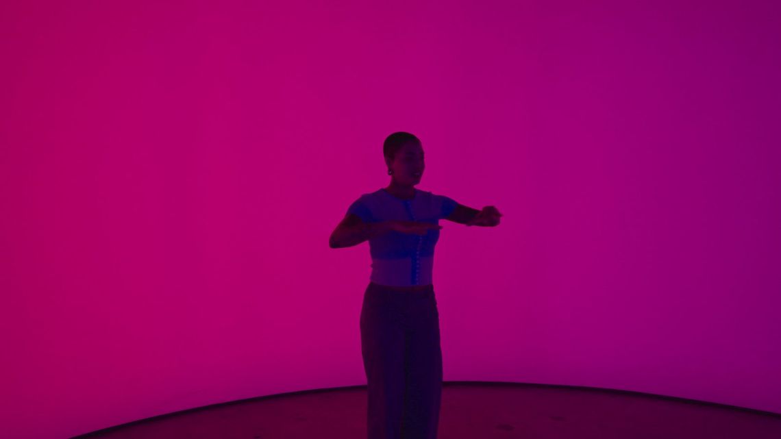 A guest with arms out against the curved field of light in hot pink.