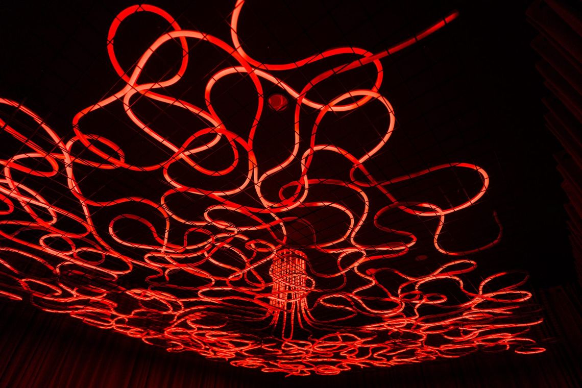 Medusa from below, red light tubes looping outward from a hanging central cluster across the dark ceiling.