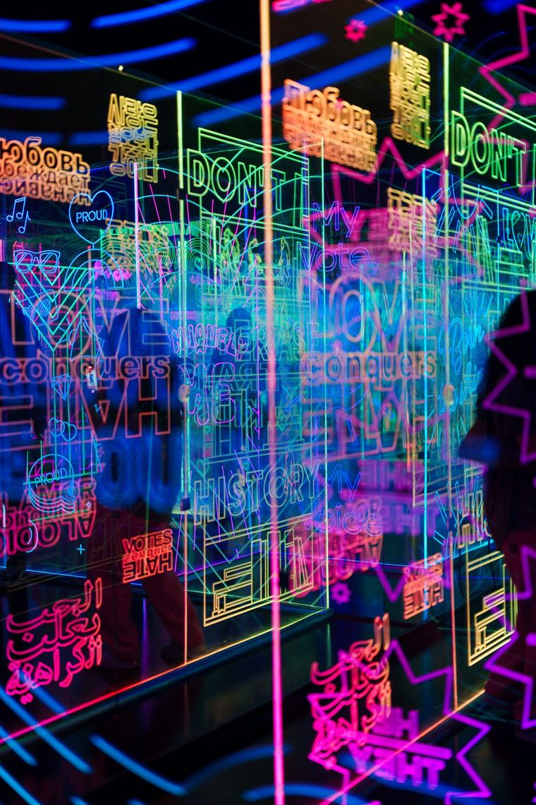 Layers of lit acrylic panels in GAZE, etched with words like LOVE, PROUD and HISTORY in several languages.
