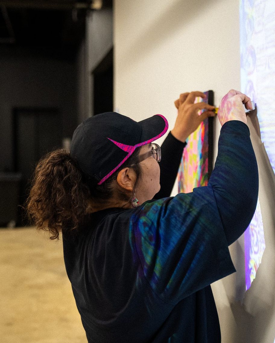 Ursula Zavala in a cap and dark jacket hanging a small painting on the gallery wall