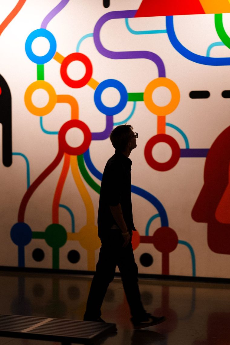 A guest walking past a white mural of rainbow lines and circles in Walls Within, Portland.