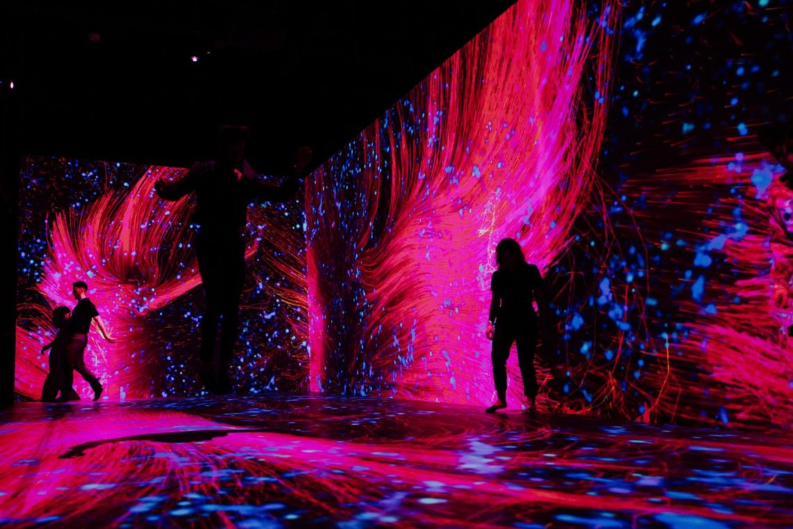 Guests in silhouette move among walls of streaming red and pink light in Quantum Trampoline.