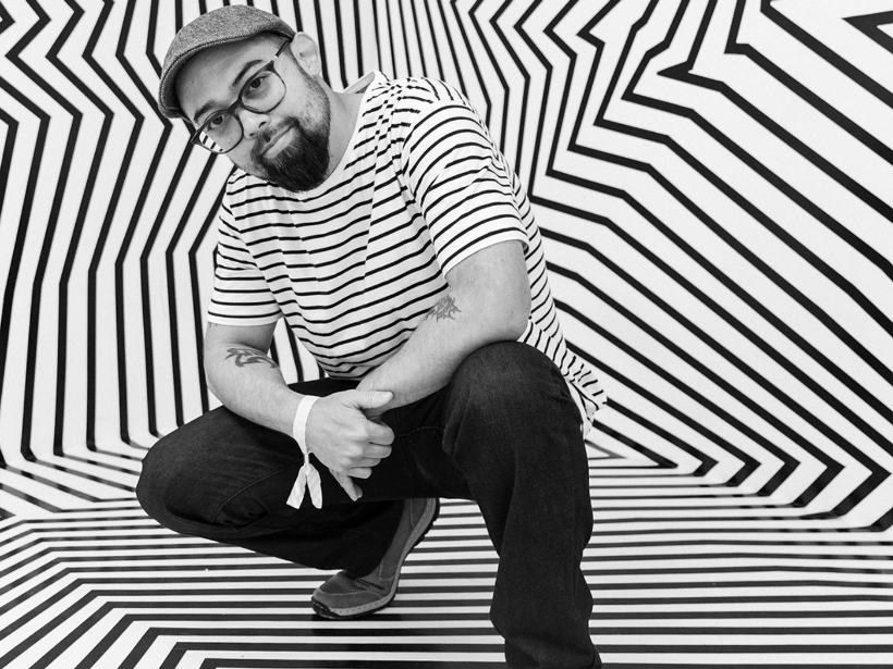 Darel Carey crouching inside a black-and-white geometric tape installation.