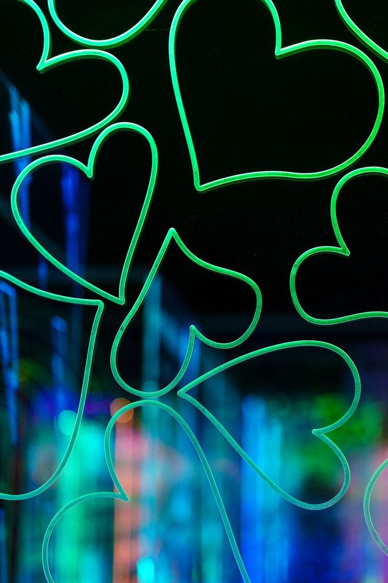 Green glowing hearts etched across an acrylic panel in GAZE, blue light blurred behind them.