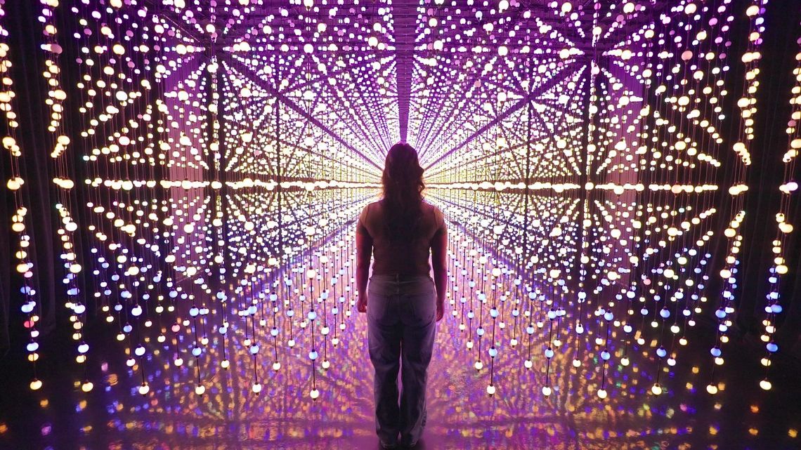 A guest in silhouette at the centre of Unknown Atmospheres, San Antonio, lines of pink and gold bulbs radiating toward her.