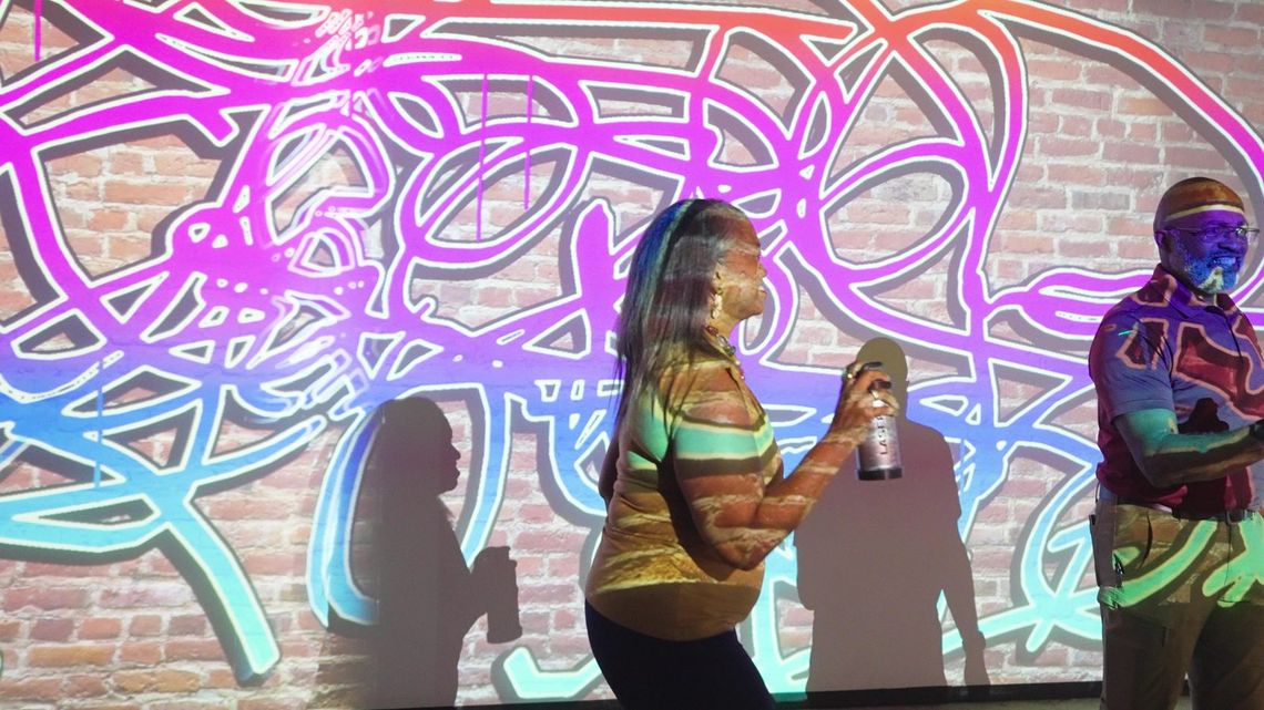 A guest sprays light across the projected brick, magenta and blue scribbles all around her.