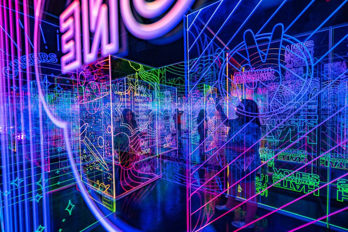 Guests walk among rows of glowing acrylic panels in GAZE, etched with words and drawings in blue, green and pink.