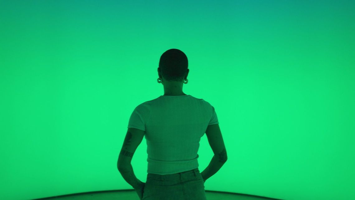 Seen from behind, a guest stands hands on hips before the curved fabric glowing green.