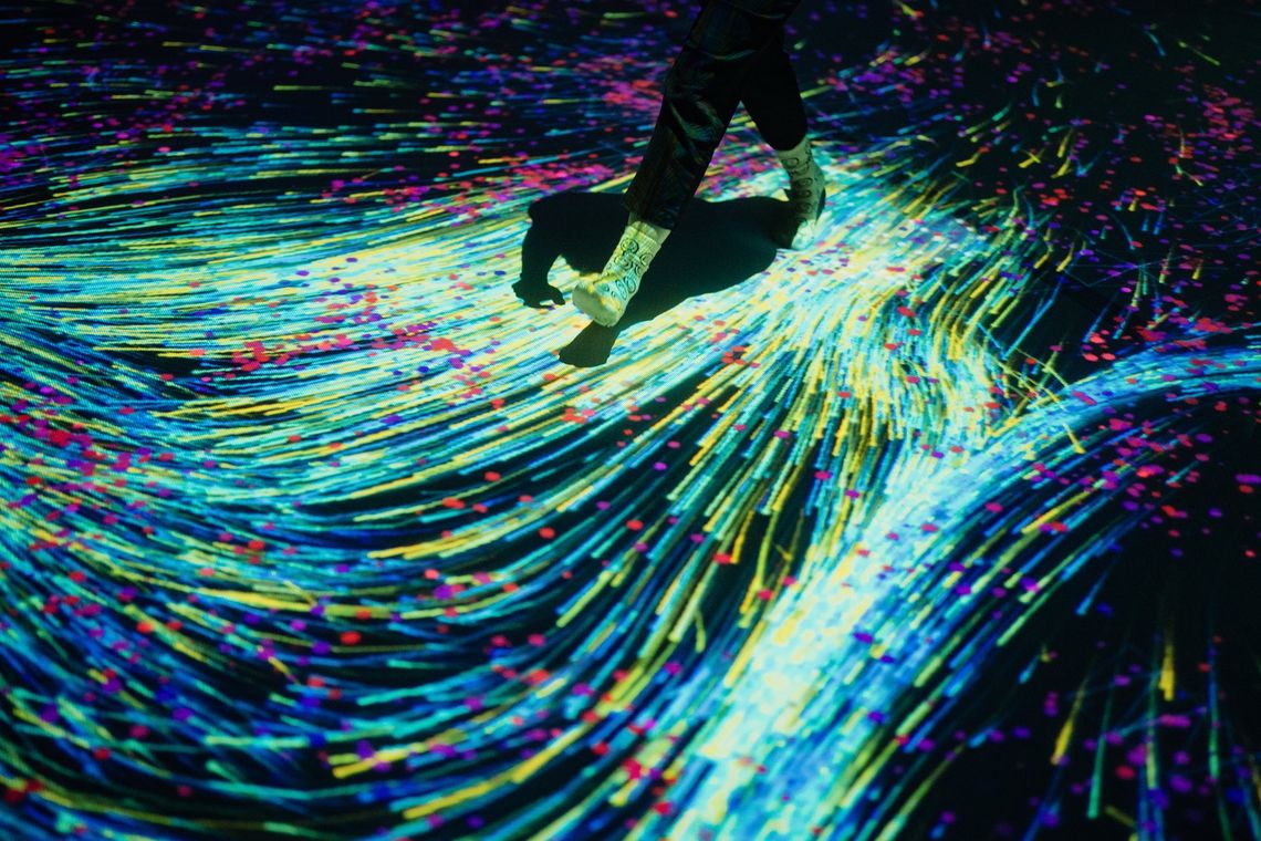 A guest steps across a floor of swirling yellow, blue and red light streaks in Quantum Trampoline.