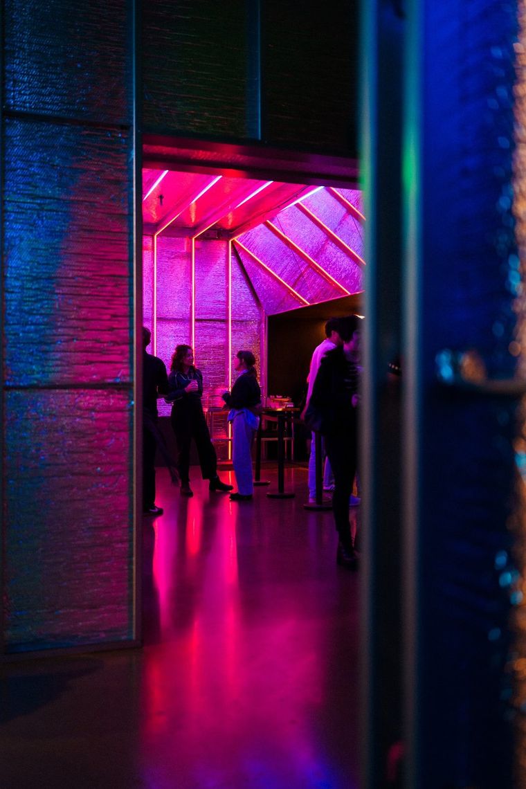 Guests gathered at a doorway glowing magenta, seen from a dark blue hallway.