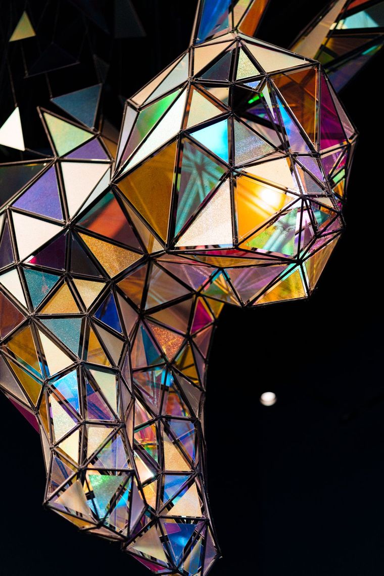 The Down the Rabbit Hole sculpture in profile against a dark ceiling, its dichroic panels glowing gold, blue and pink.