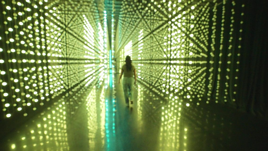 A guest walking a corridor of yellow-green light in Unknown Atmospheres, San Antonio.