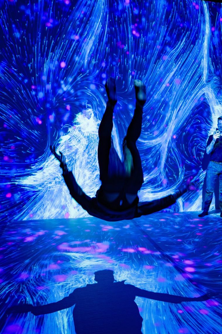 A guest dives backward, arms out, through swirling blue light in Quantum Trampoline.