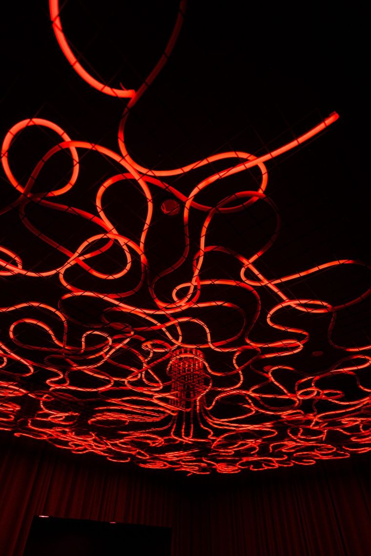 Red tubes of light looping from the Medusa chandelier across the Portland entry ceiling, the red velvet curtains of the entry hanging below.