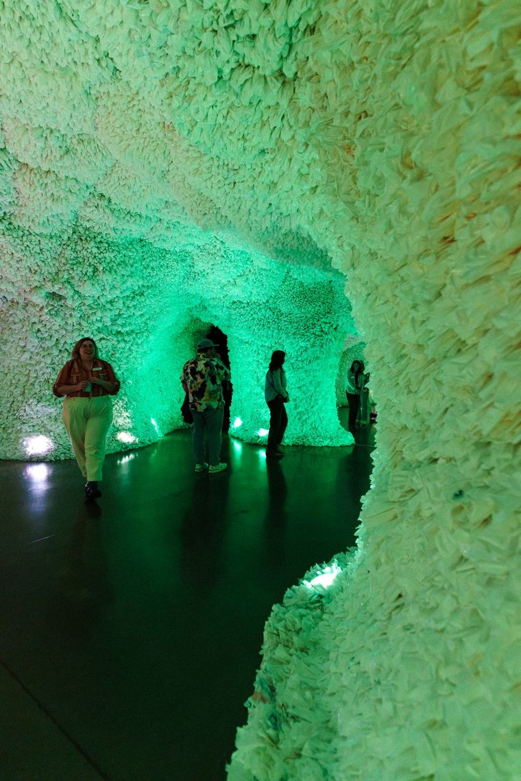 Guests walk through a green-lit tunnel in Rainbow Cave, its walls built from layers of white plastic.
